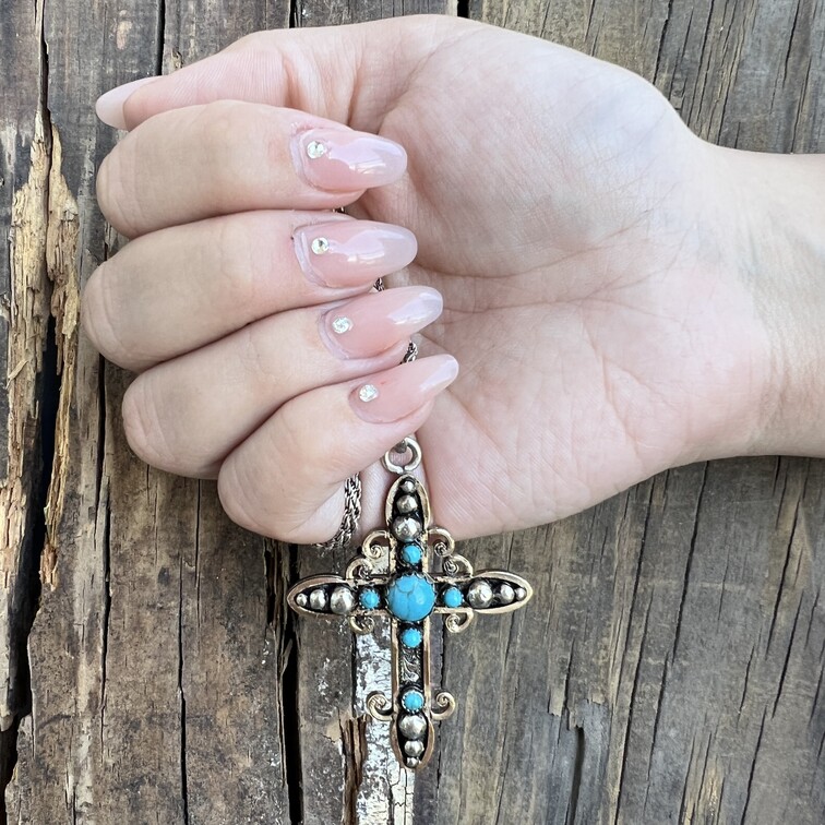 A turquoise cross pendant in a femenine hand